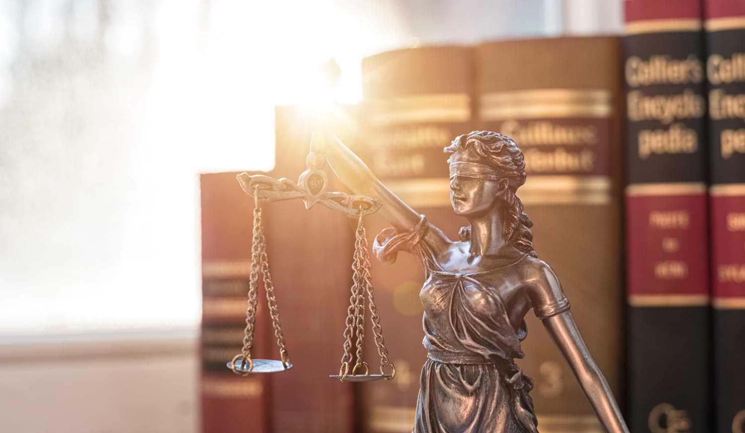Bronzestatue der Lady Justice mit einer Waage in der Hand und Gesetzesbüchern im Hintergrund.